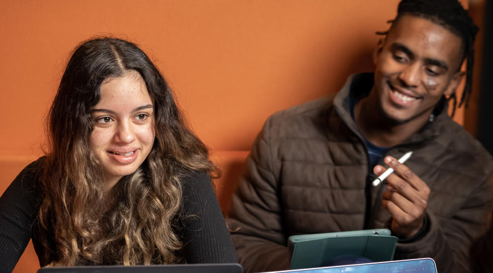 Image of a group of international students sat at a table talking with their laptops