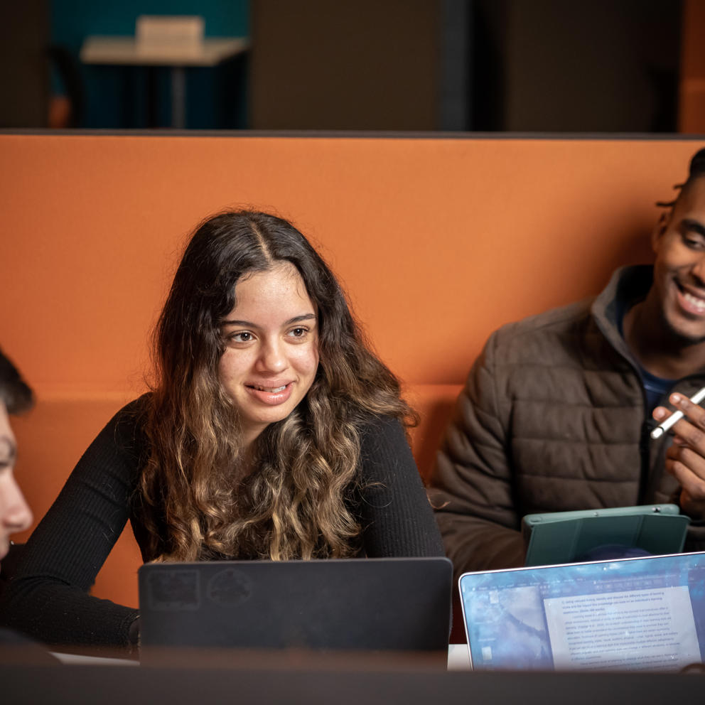 Image of a group of international students sat at a table talking with their laptops